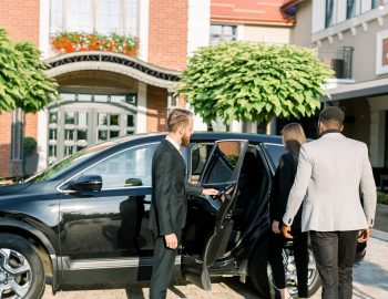 chauffeur-man-opening-car-door-for-business-couple-2021-09-04-16-23-16-utc